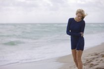Thoughtful blond woman in dress standing on windy beach — Stock Photo