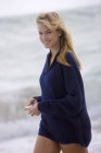 Mujer sonriente sosteniendo concha mientras camina en la playa - foto de stock