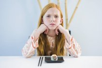 Retrato de menina de gengibre irritado sentado na mesa de jantar com sushi — Fotografia de Stock