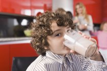 Портрет хлопчика, який п'є молоко зі скла на кухні — стокове фото