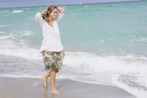 Smiling young woman walking on beach with hands in hair — Stock Photo