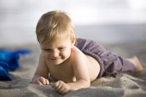 Nahaufnahme eines glücklichen Jungen, der auf Sand liegt — Stockfoto