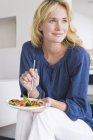 Sorrindo elegante mulher segurando prato de salada de frutas e olhando para longe — Fotografia de Stock