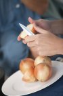 Frauenhände hacken Zwiebeln auf Teller — Stockfoto