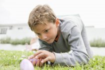 Хлопчик дивиться на пасхальне яйце, на коліна на траві — стокове фото