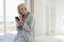 Улыбающаяся женщина с мобильного телефона в прибрежном доме — стоковое фото