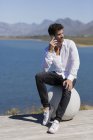 Человек сидит на каменном шаре и разговаривает по мобильному телефону в природе — стоковое фото