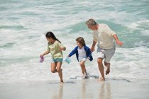 Діти грають зі своїм дідом на пляжі — стокове фото