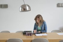 Жінка розбирає рахунки за дерев'яним столом в сучасній квартирі — стокове фото
