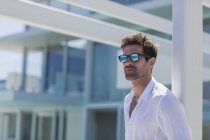 Крупним планом впевнений стильний чоловік у сонцезахисних окулярах перед сучасною будівлею — стокове фото