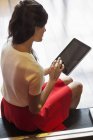 Élégante jeune femme utilisant une tablette numérique tout en étant assis dans la chambre — Photo de stock