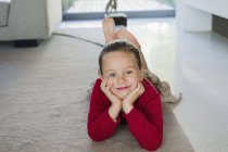 Ritratto di bambina sorridente sdraiata su tappeto a casa — Foto stock