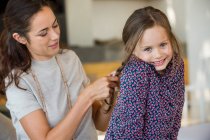 Smiling woman braiding her daughter's hair — Stock Photo