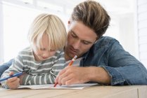 Father and son doing homework on table at home — Stock Photo