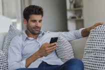 Lächelnder Mann mit Handy auf Sofa zu Hause — Stockfoto