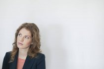 Retrato de mulher pensativa na jaqueta olhando para cima contra a parede branca — Fotografia de Stock