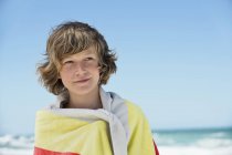 Menino adolescente pensativo envolto em toalha em pé na praia — Fotografia de Stock