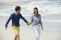Couple walking on sandy beach holding hands — Stock Photo