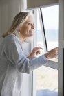 Lächelnde Seniorin blickt durch Fenster im Haus — Stockfoto
