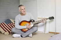 Thoughtful man playing guitar on floor at home — Stock Photo