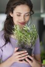 Mulher sorridente cheirando vaso de alecrim planta — Fotografia de Stock