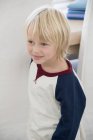 Gros plan d'un petit garçon heureux aux cheveux blonds regardant loin à l'intérieur — Photo de stock