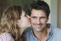 Primer plano de la mujer joven besando novio sonriente en la mejilla - foto de stock