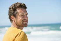 Nachdenklicher Mann lächelt vor winkendem Meer — Stockfoto