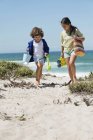 Ragazza e ragazzo a piedi sulla spiaggia di sabbia con giocattoli — Foto stock