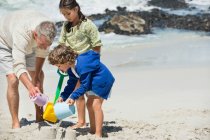 Kinder spielen mit ihrem Großvater am Strand — Stockfoto