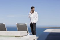 Впевнений чоловік говорить на мобільному телефоні на терасі на березі озера — стокове фото