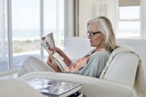 Женщина сидит на диване и читает журнал дома — стоковое фото