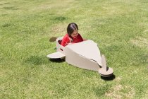 Kleines Mädchen spielt mit Pappflugzeug auf Rasen — Stockfoto