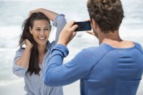 Homem tirando foto da esposa com telefone celular na praia — Fotografia de Stock