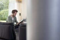 Hombre usando tableta digital en el sofá en casa - foto de stock