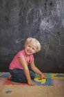 Sorrindo bonito menina brincando com quebra-cabeça número na frente de um quadro negro — Fotografia de Stock