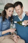 Smiling couple pouring wine in glass in kitchen — Stock Photo