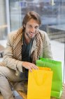 Retrato del hombre sonriente sentado en el salón del aeropuerto con bolsas de compras - foto de stock