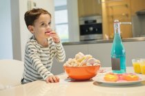 Kleiner Junge isst Snack in Schüssel auf Tisch in Küche — Stockfoto
