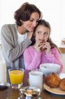 Chica desayunando junto a su madre en un mostrador de cocina - foto de stock