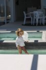 Cute thoughtful baby girl standing in infinity pool and looking away — Stock Photo