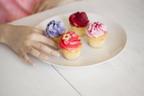 Hand of girl taking with cupcake from plate on table — Stock Photo