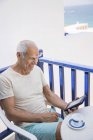 Hombre mayor feliz usando una tableta digital en el balcón - foto de stock