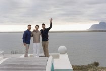 Retrato de tres felices amigos varones de pie a orillas del lago - foto de stock