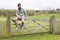 Чоловік сидить на дерев'яному паркані в сільській місцевості і думає — стокове фото