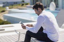 Hombre usando la tumbona del teléfono inteligente en la terraza - foto de stock