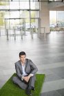 Businessman relaxing on grass mat in office lobby — Stock Photo