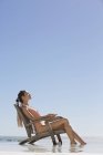 Elegante entspannte Frau sitzt auf Stuhl am Strand — Stockfoto