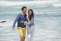 Paar spaziert am Strand mit welligem Meer im Hintergrund und blickt in die Kamera — Stockfoto