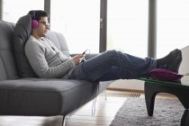 Man listening to music with MP3 player on sofa in living room — Stock Photo